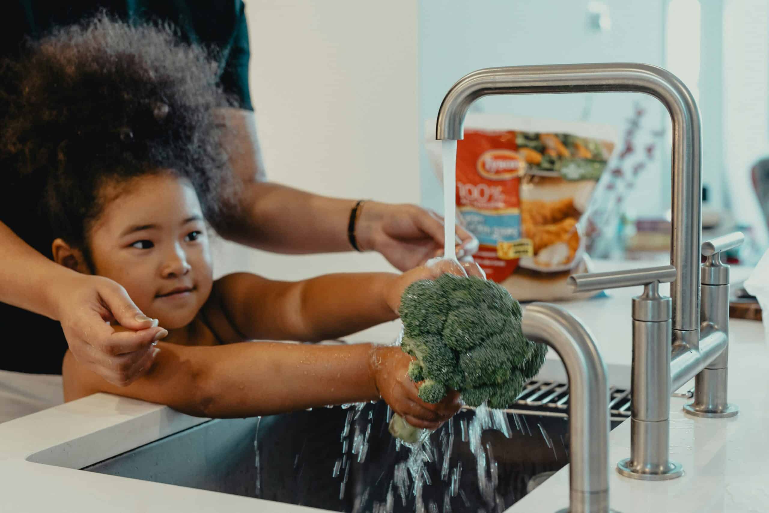 Girl washing broccoli in kitchen